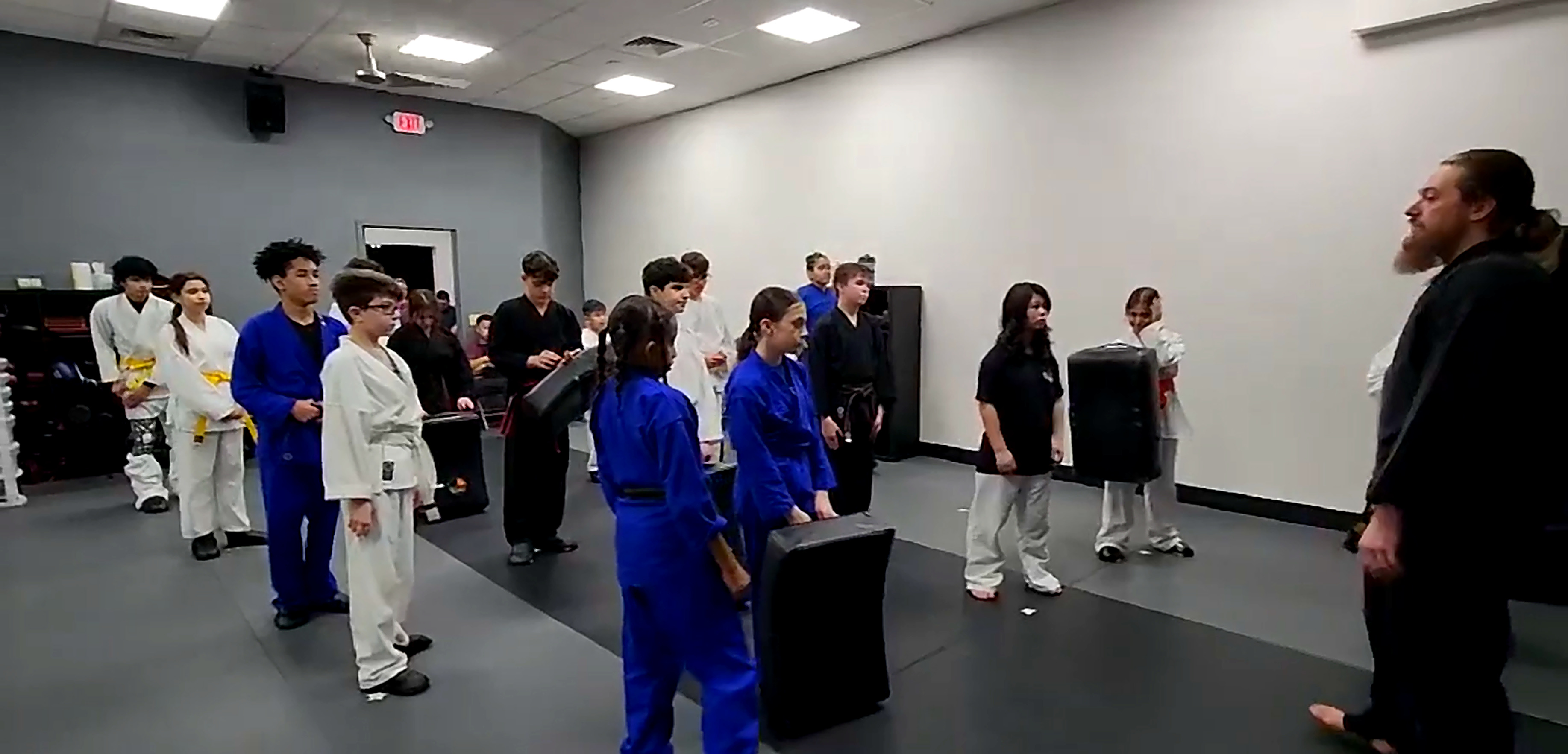 Older kids class lined up with kicking pads listening to their martial arts instructor